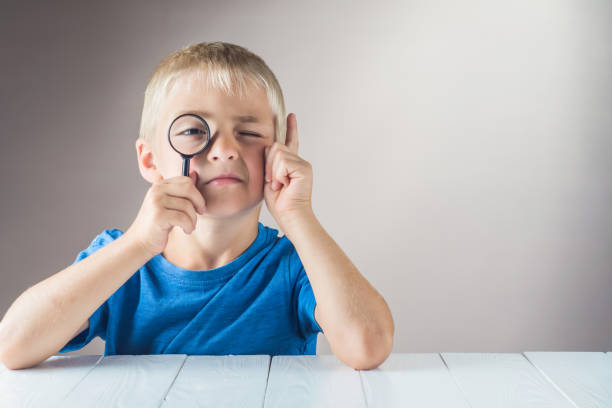 Curious boy with a clever face looks through the magnifying glass and lifts his index finger up. The concept of logical thinking.