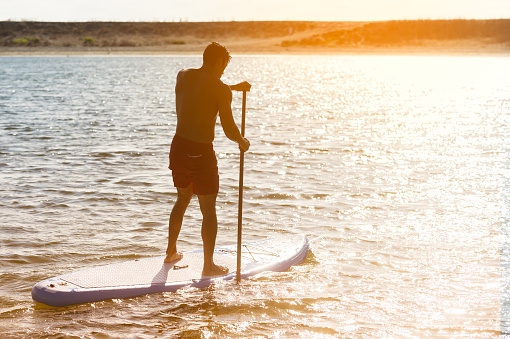 Man Stand Up Paddle Boarding into the warm sunset.