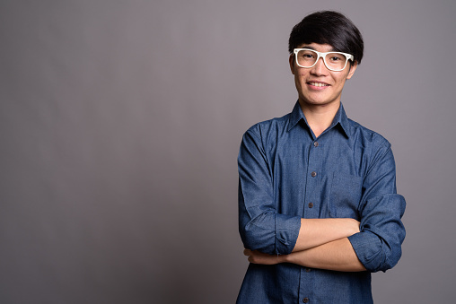Studio shot of young Asian man wearing smart casual clothes and eyeglasses against gray background horizontal shot