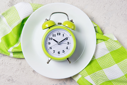 Green alarm clock with bells on the plate, lunch time concept, top view with copy space