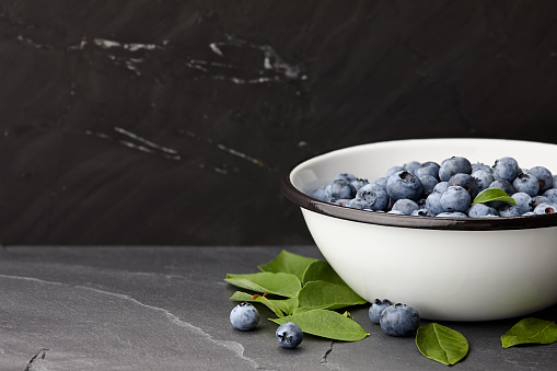 Fresh ripe blueberries with leaves bowl on black stone countertop