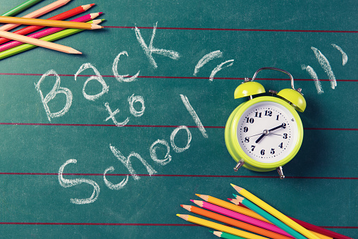 Retro alarm clock and colored pencils on the chalkboard with back to school text, top view, filter