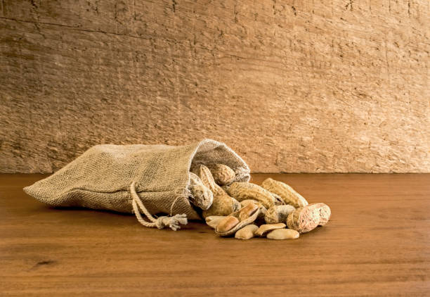 borsa a tela di arachidi nel guscio su uno sfondo di legno rustico. - peanut bag nut sack foto e immagini stock