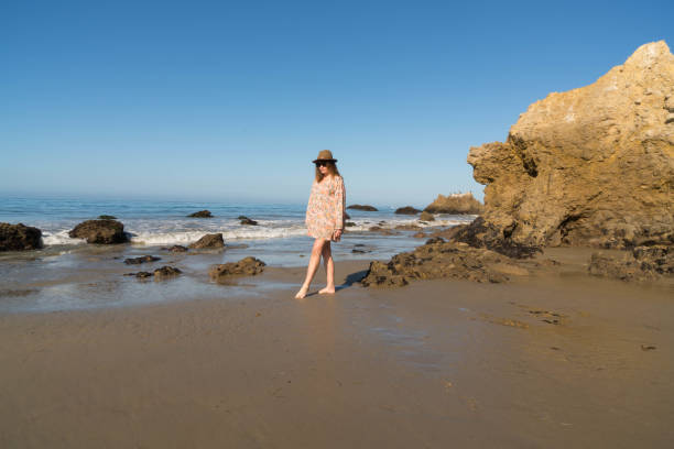 Woman walks along sandy Beach A woman walks and reflects along a sandy beach. rock sea malibu silhouette stock pictures, royalty-free photos & images