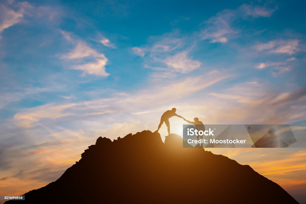 Silhouette of couple teamwork  hiker helping each other on top of mountain Two People Stock Photo