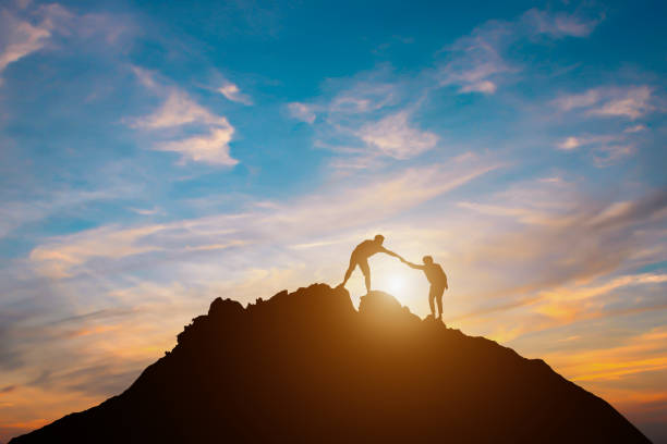 Silhouette of couple teamwork  hiker helping each other on top of mountain stock photo