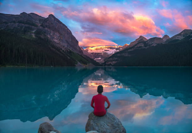 hombre se siente sobre la roca mirando las nubes de mañana de lago louise con reflejos - landscape canada mountain rock fotografías e imágenes de stock