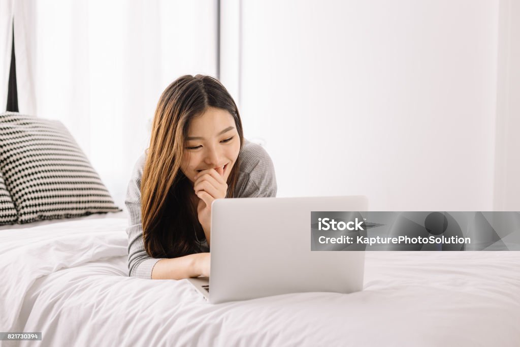 Young Asian Girl using laptop on the bed Laptop Stock Photo