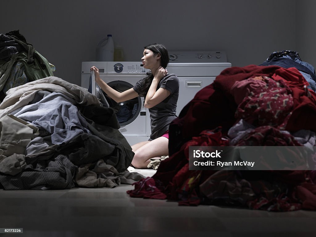 Woman sitting in laundry room, overwhelmed  Chaos Stock Photo