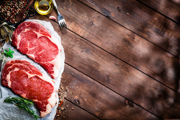 Fresh beef steak fillets with cooking abd seasoning ingredients on rustic wooden table Top view of two fresh beef steak fillets on butcher's paper with some cooking and seasoning ingredients placed at the left border of a rustic wooden kitchen table leaving useful copy space for text and/or logo. Predominant colors are brown and red. DSRL studio photo taken with Canon EOS 5D Mk II and Canon EF 100mm f/2.8L Macro IS USM abd stock pictures, royalty-free photos & images