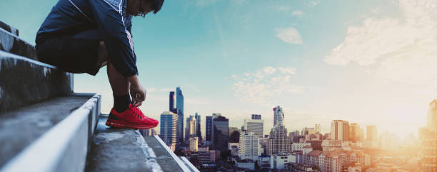 istock Panoramic Asian Guy Tying Running Shoe, Preparing for Running, with City background in Sunrise 821746028