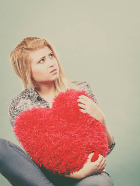 istock Sad woman holding red pillow in heart shape 821760170