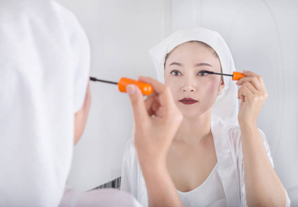 istock woman looking mirror and applying mascara on her eyelashes 821768208
