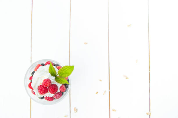 Layered dessert with raspberry cream cheese in glass on white wooden table. View from above.