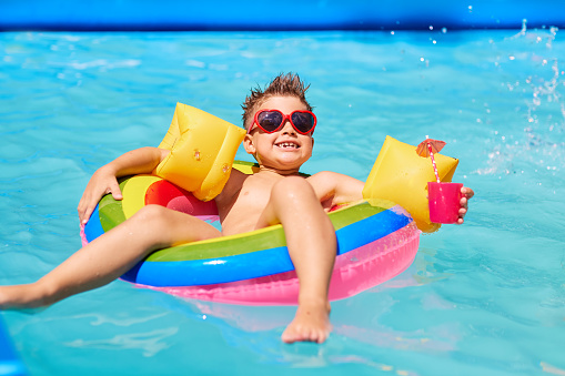 Happy child in sunglasses in the pool with a cocktail. Concept of summer holidays.