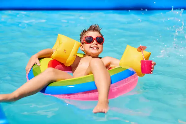 Photo of Happy child in sunglasses in the pool with a cocktail.