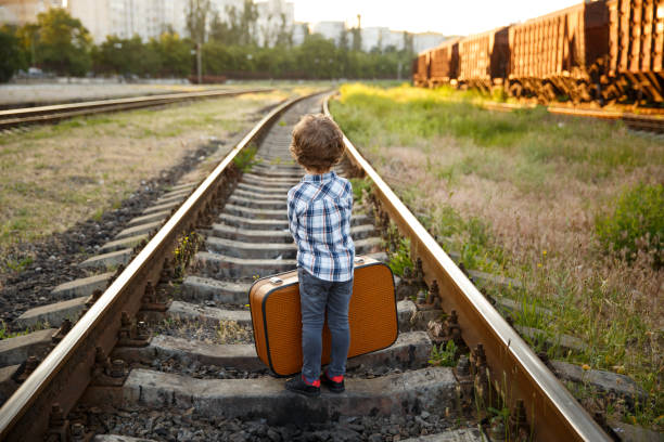 istock Young boy carrying suitcase standing on railways 821807170