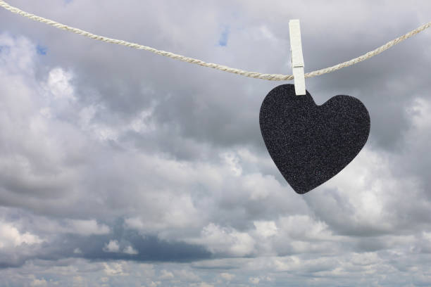 istock Black Heart paper hanging on a brown hemp rope on rain clouds background. 821809148
