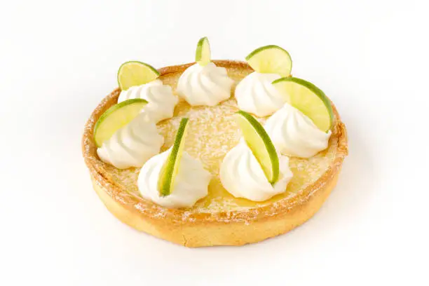 Closeup of a homemade lemon tart decorated with meringue swirls and lime slices on white background.