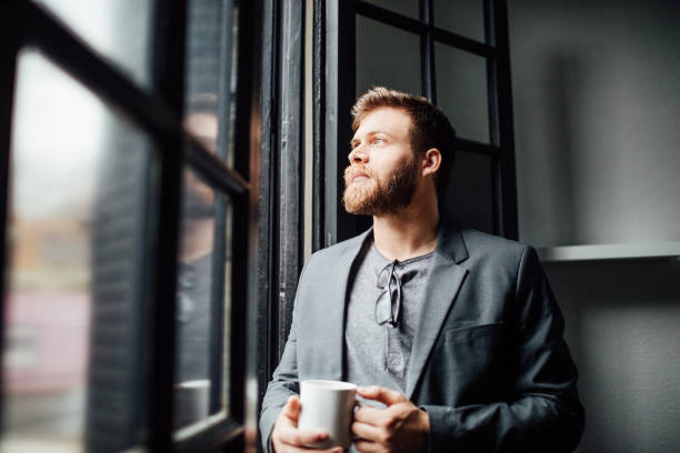 istock Thoughtful young businessman standing by office window 821841370