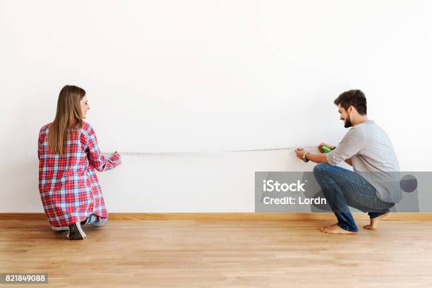 Couple In Empty Apartment Measuring Walls Stock Photo - Download Image Now - Measuring, Empty, Couple - Relationship