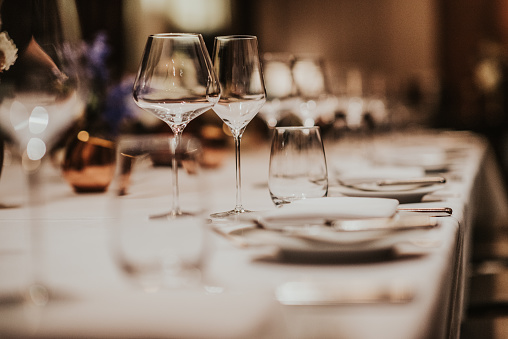 Table arrangement for a special event such a wedding or a celebration with perfectly lined up cutlery and dinnerware with cone-folded cotton napkins, enhanced by floral centerpieces and white candles.