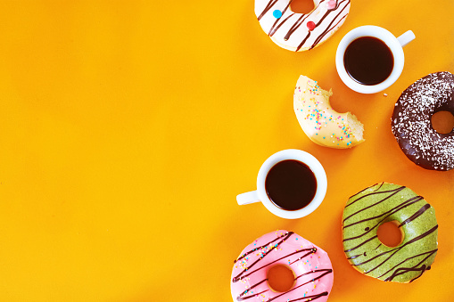 Pistachio, chocolate, vanilla, strawberry donuts and two cups of espresso over yellow background.