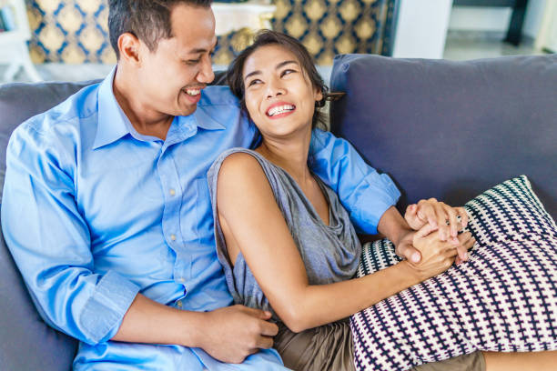 istock Thai couple portrait sitting on the couch, talk and laugh. Modern style interior. 821877014