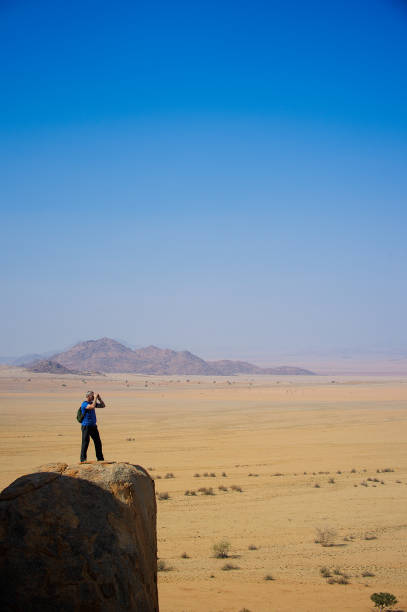 istock Man with binoculars standing high up on a desert rock 821877572