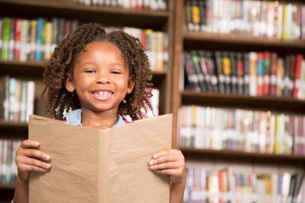 istock African descent little girl in school library reading book. 821889804