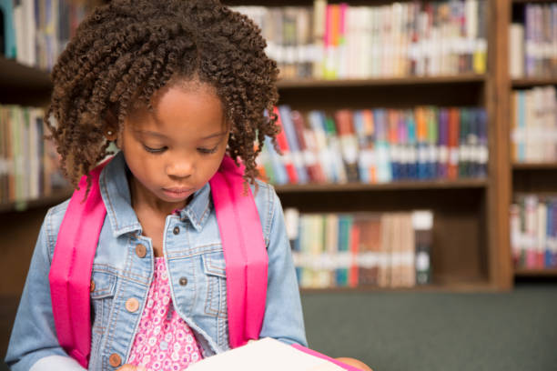 istock African descent little girl in school library reading book. 821894232