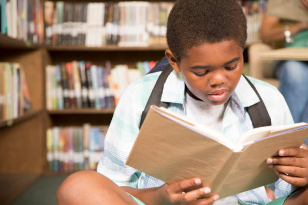 istock African descent boy in school library with book. 821894496