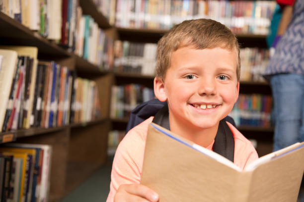 istock Caucasian little boy reading books in school library. 821894606