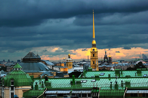 Gold painted spires of Peter and Paul Cathedral over wet green roofs against overcast sunset sky in Saint Petersburg, Russia