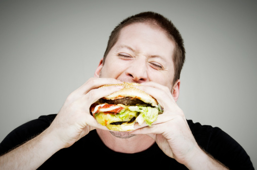 Happy white guy in yellow hoodie eating hamburger on blue background