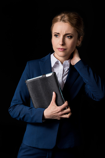 tired middle aged businesswoman holding digital tablet and looking away isolated on black