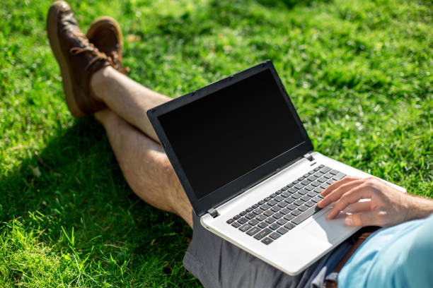 istock Cropped shot of man using laptop with blank screen while sitting on green grass 821924230