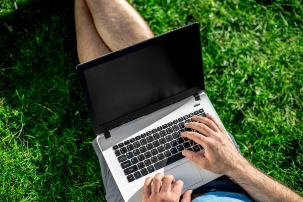 istock Cropped shot of man using laptop with blank screen while sitting on green grass 821926632