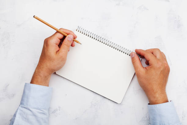 istock Lefty writes in clean notebook on white table top view. International Lefthanders Day. 821931518