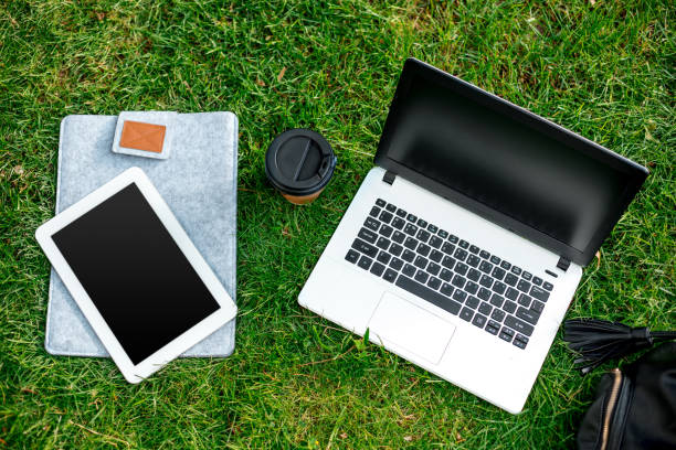 istock Laptop computer on green grass with coffee cup, bag and tablet in outdoor park 821933558