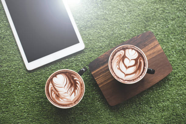 Cups of coffee with beautiful Latte art on green background ans computer laptop stock photo