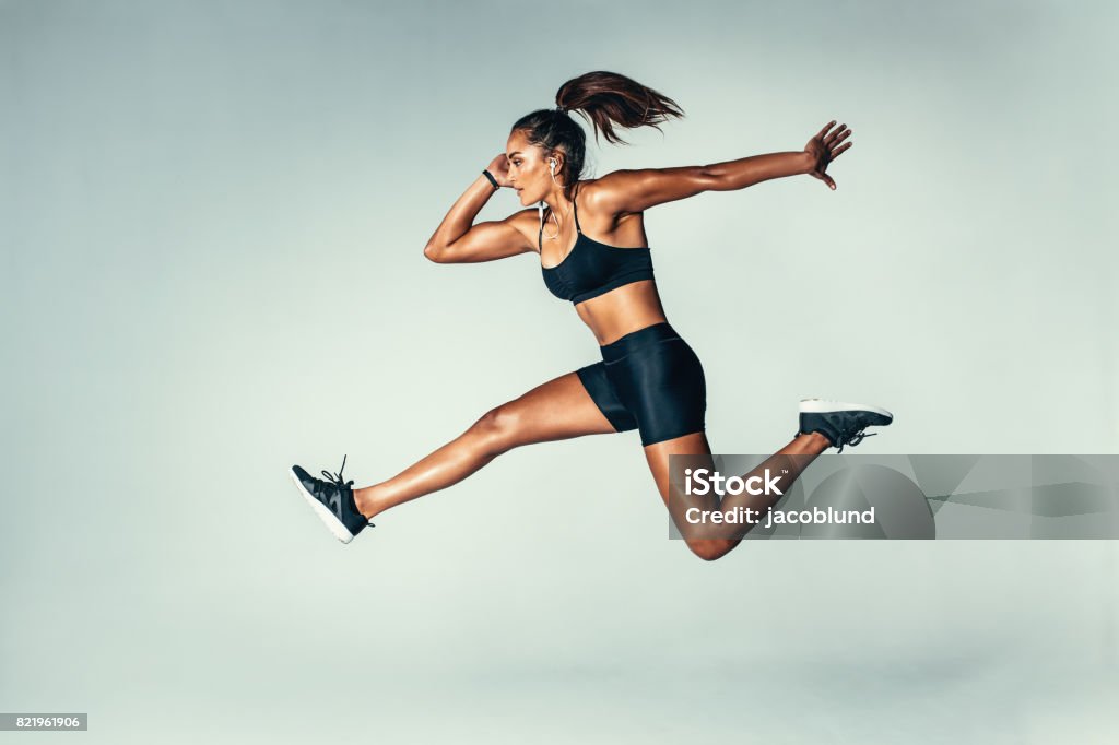 Fit young woman jumping in air Side view of fit young woman jumping against grey background. Female model in sports wear jumping in air. Women Stock Photo