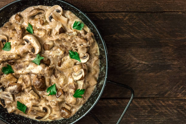 Mushroom beef stroganoff in pan with copy space A closeup of a mushroom beef stroganoff, with cremini and champignons, in a frying pan, shot from above on a dark rustic texture with a place for text crimini mushroom stock pictures, royalty-free photos & images