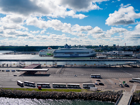 An elevated view over the ferry port in Tallinn, capital of Estonia on an intermittently cloudy day. Amongst the waiting ferries is a ‘Tallink’ ferry and by the quayside a row of tour buses waits for passengers.