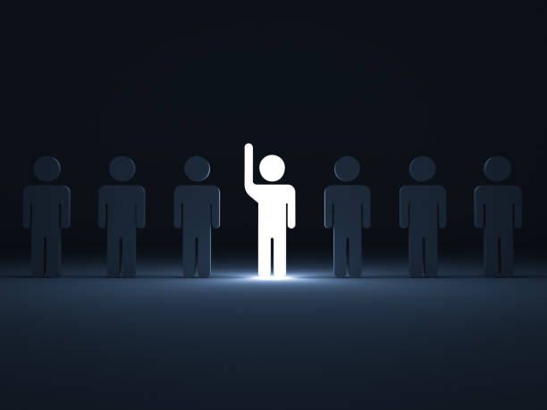 istock Stand out from the crowd and different concept , One glowing light man raising his hand among other dim people in the row on dark blue background with shadows . 3D rendering 822055178