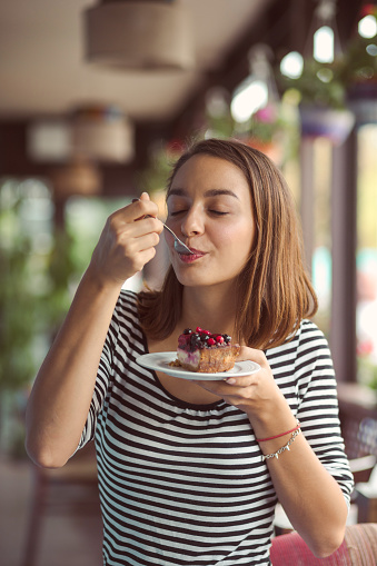 Young woman eating delicious dessert at city cafe. Cafe city lifestyle. Casual portrait of teenager girl