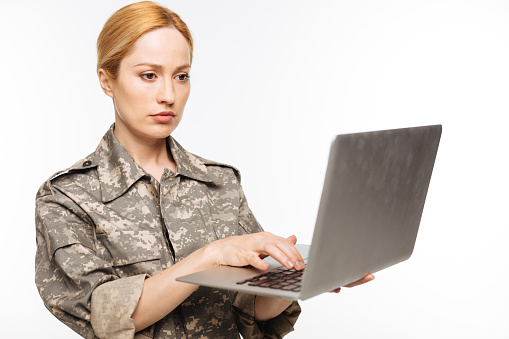 Military technologies. Attractive resolute admirable woman using protected connection while reading a message on her laptop and standing isolated on white background