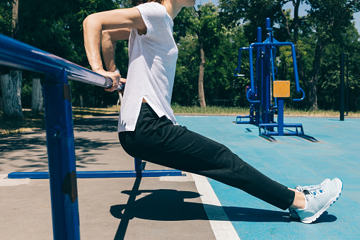 Close-up of a young athletic woman doing exercises for the triceps on the playground in the summer. Concept of a healthy lifestyle.