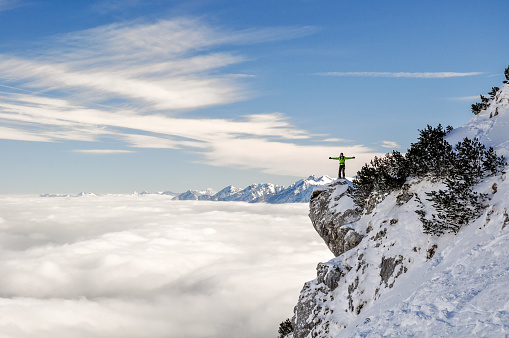 Stunning view of a hiker standing on a steep cliff near the Bavarian town of Garmisch Partenkirchen near Zugspitze mountain in Germany. Beautiful snow landscape in winter. Deep snow off piste slope.
