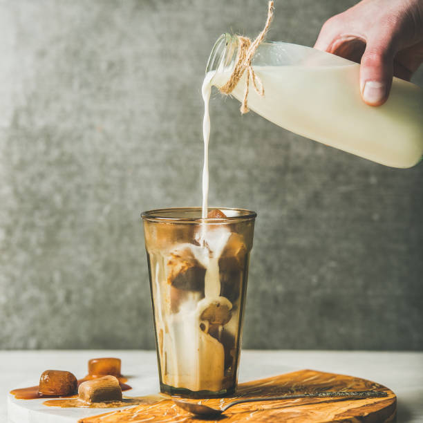 man's hand pouring milk to cold latte coffee cocktail - caramel latté coffee cafe macchiato imagens e fotografias de stock